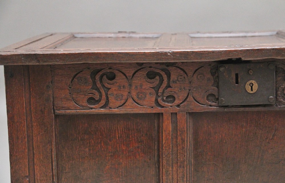 An early 18th-century dark oak coffer featuring three sunken front panels, a hand-carved frieze, and a central iron lock plate. View X