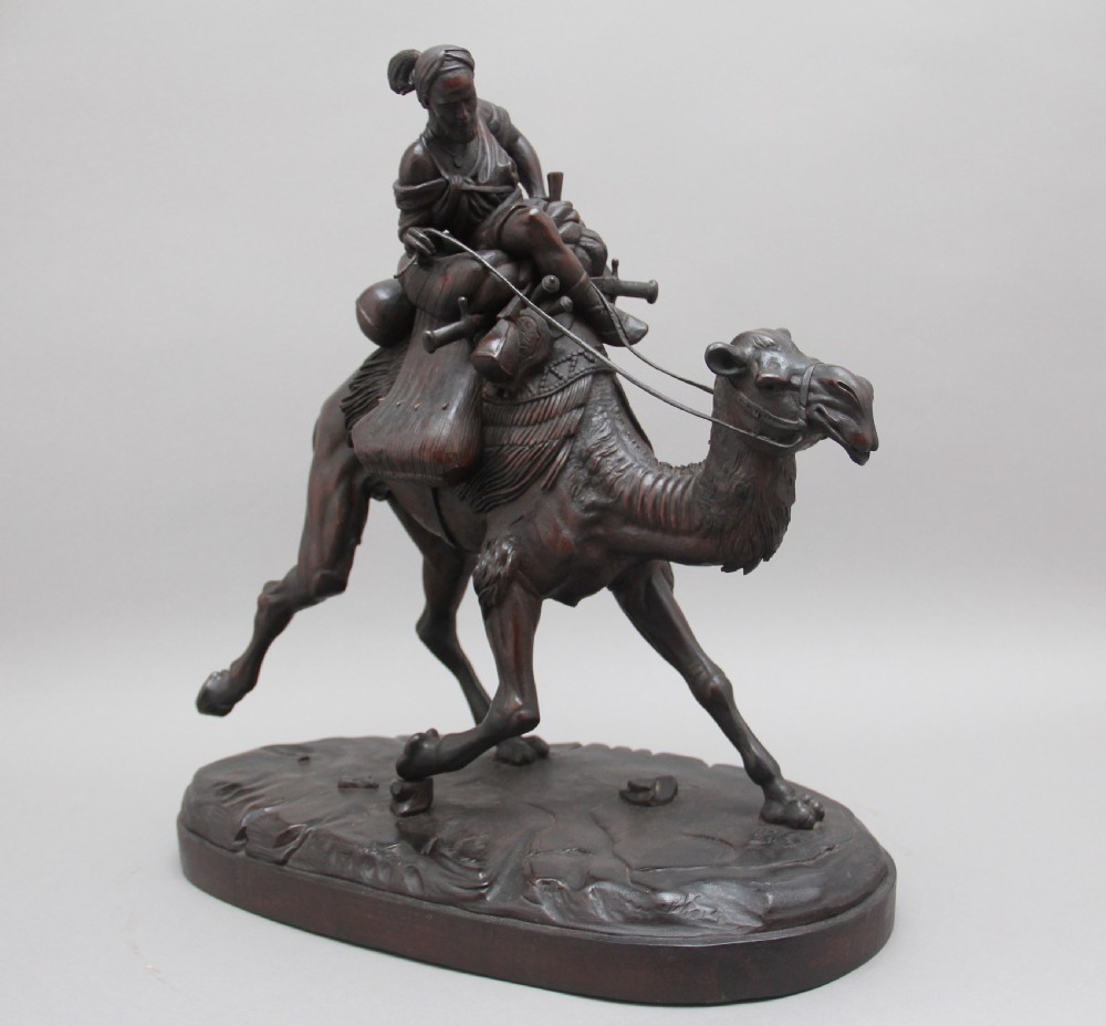 A 19th-century dark carved wood sculpture depicting a figure mounted on a striding camel upon an oval base.