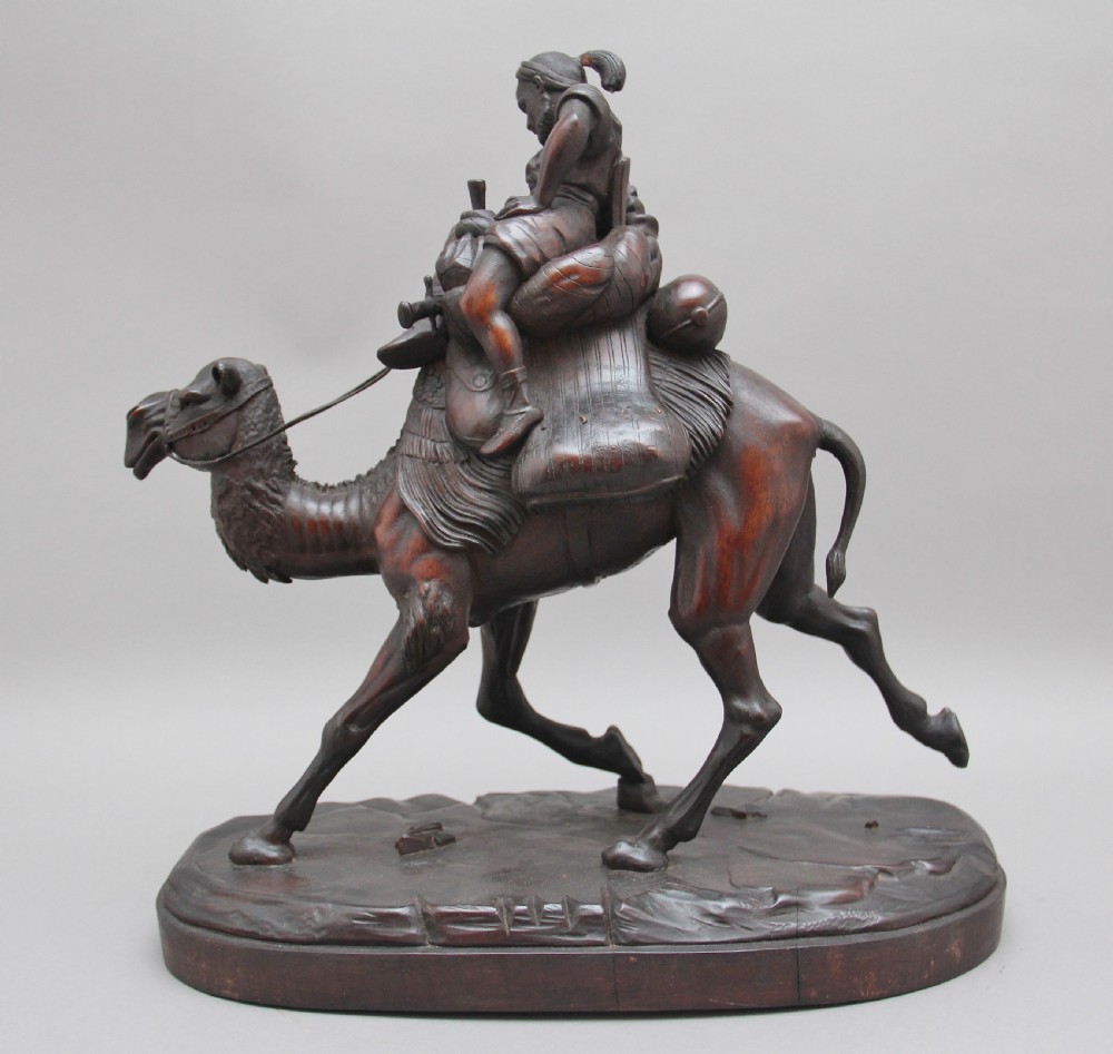 A 19th-century dark carved wood sculpture depicting a figure mounted on a striding camel upon an oval base. View VI