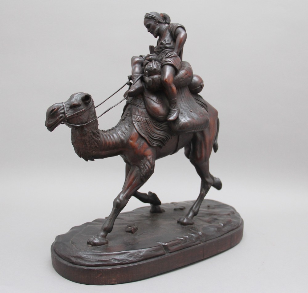 A 19th-century dark carved wood sculpture depicting a figure mounted on a striding camel upon an oval base. View VII