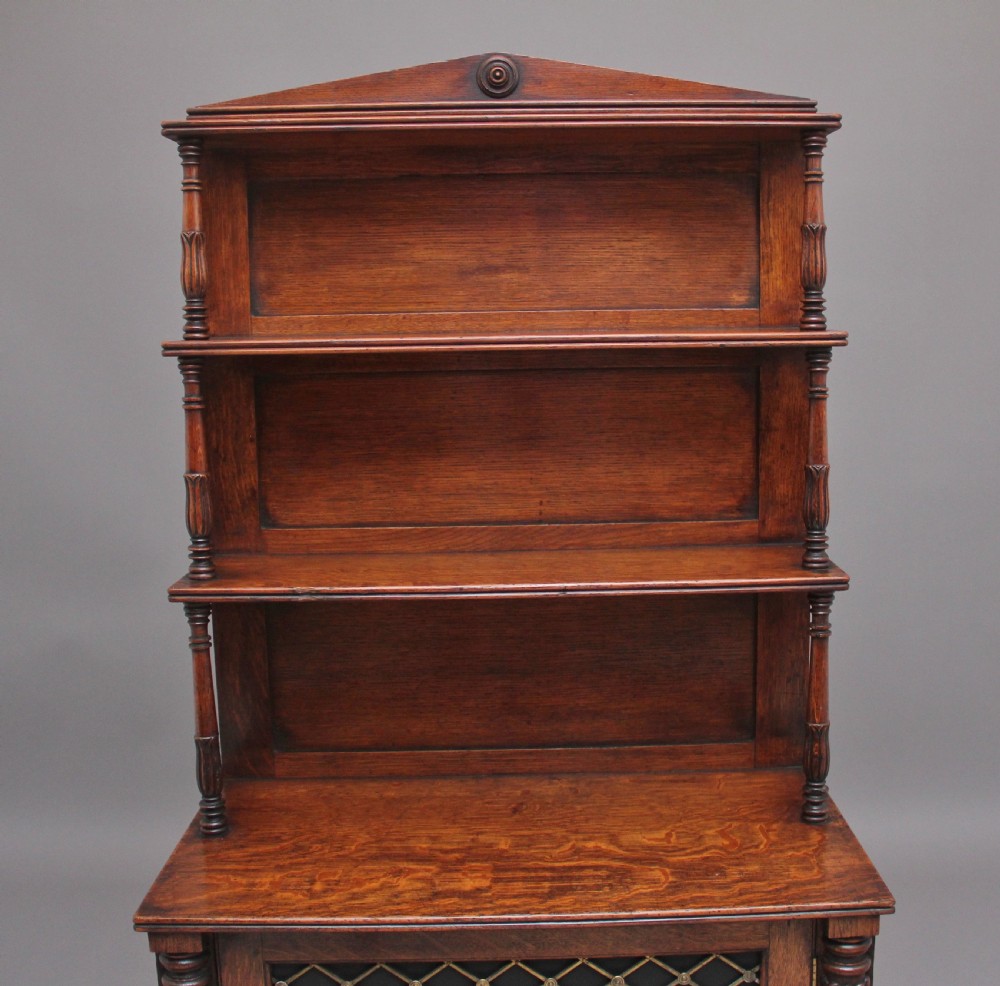 An early 19th-century oak bookcase featuring three open upper shelves topped with a pediment, above a lower cabinet with a brass grille door and spiral twist side columns. View VI
