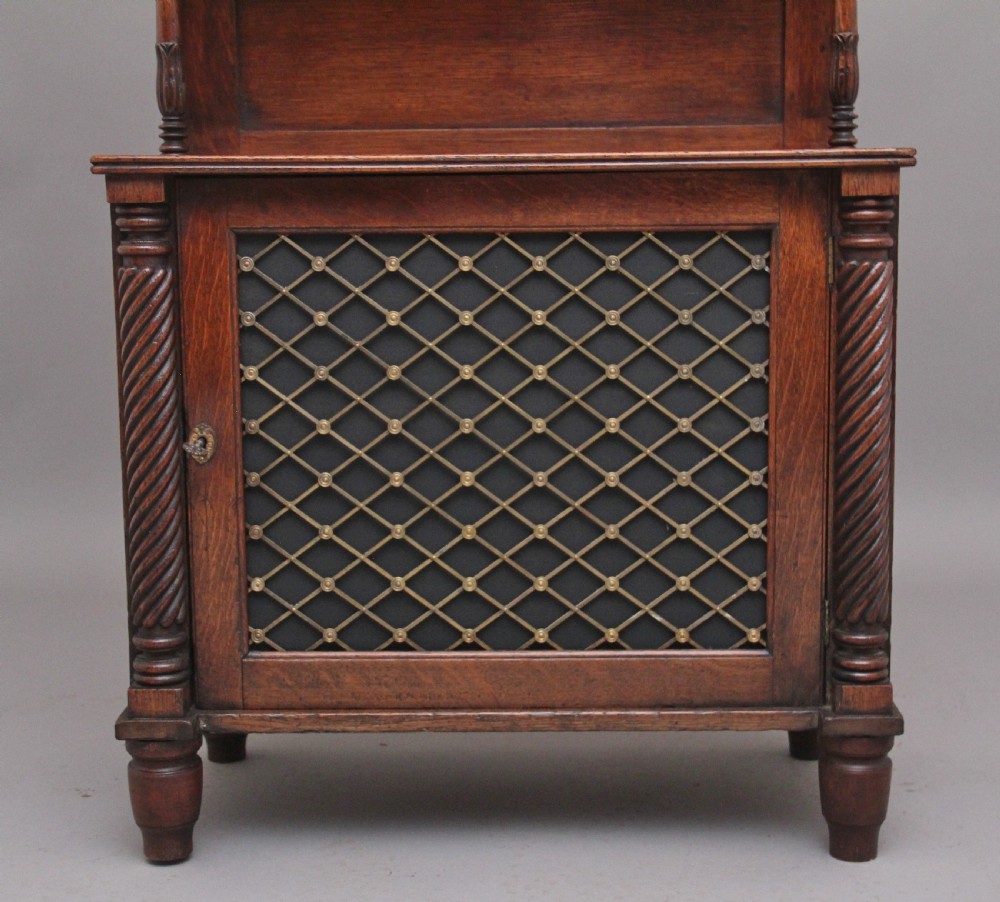 An early 19th-century oak bookcase featuring three open upper shelves topped with a pediment, above a lower cabinet with a brass grille door and spiral twist side columns. View VII