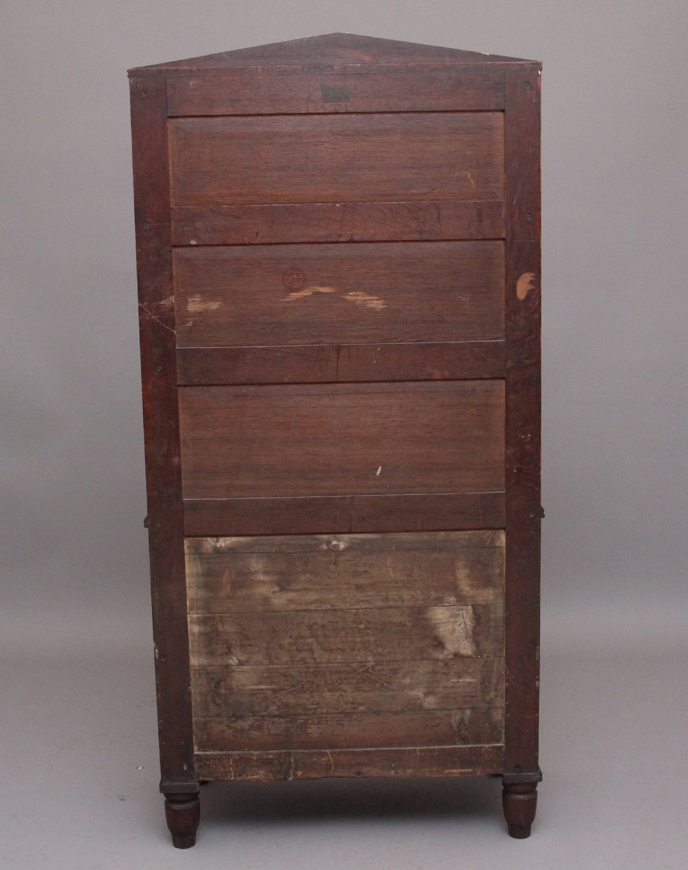 An early 19th-century oak bookcase featuring three open upper shelves topped with a pediment, above a lower cabinet with a brass grille door and spiral twist side columns. View X