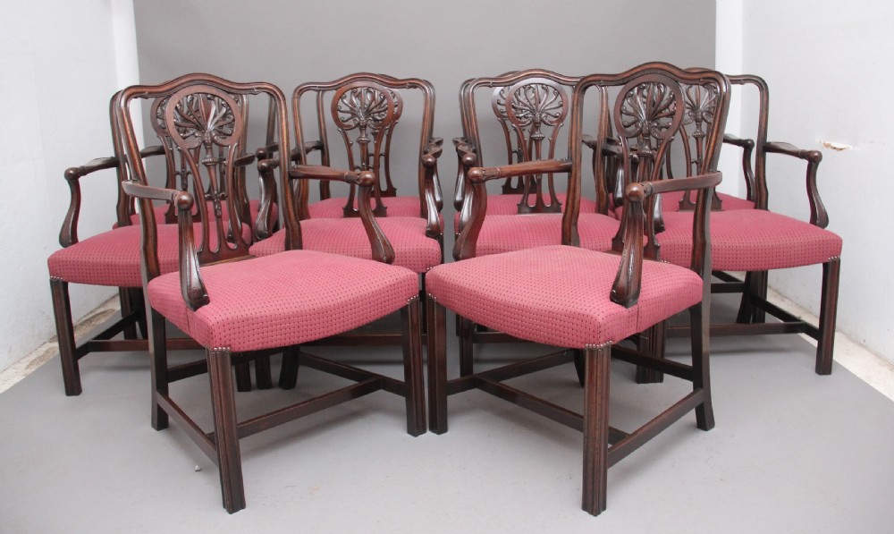 A set of dark mahogany dining armchairs featuring intricate anthemion carved back splats, curved arms, and pink patterned upholstered seats.