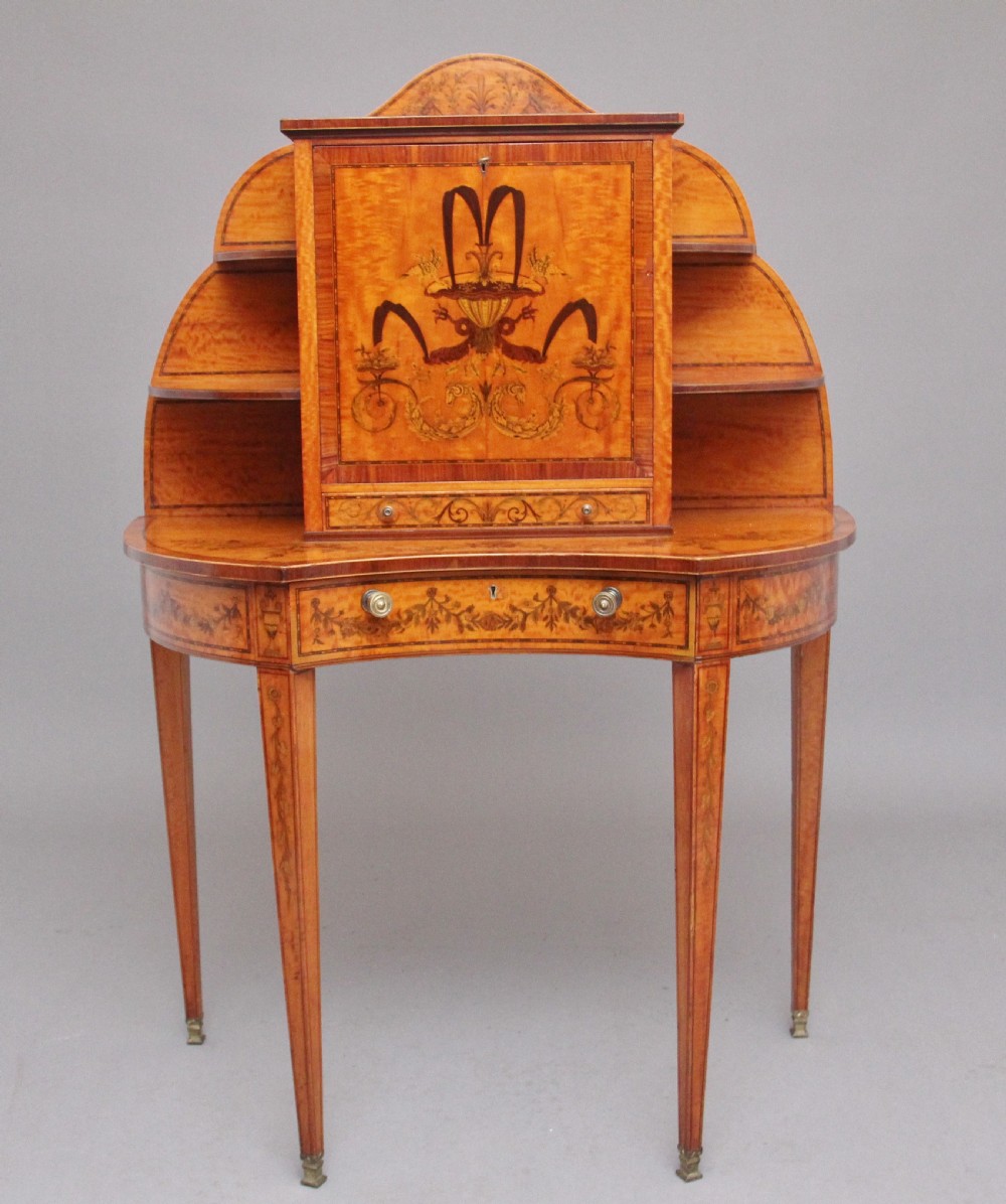 A 19th-century Sheraton revival satinwood writing desk featuring inlaid urn marquetry motifs, stepped side shelves, a central door compartment, and slender tapered legs.