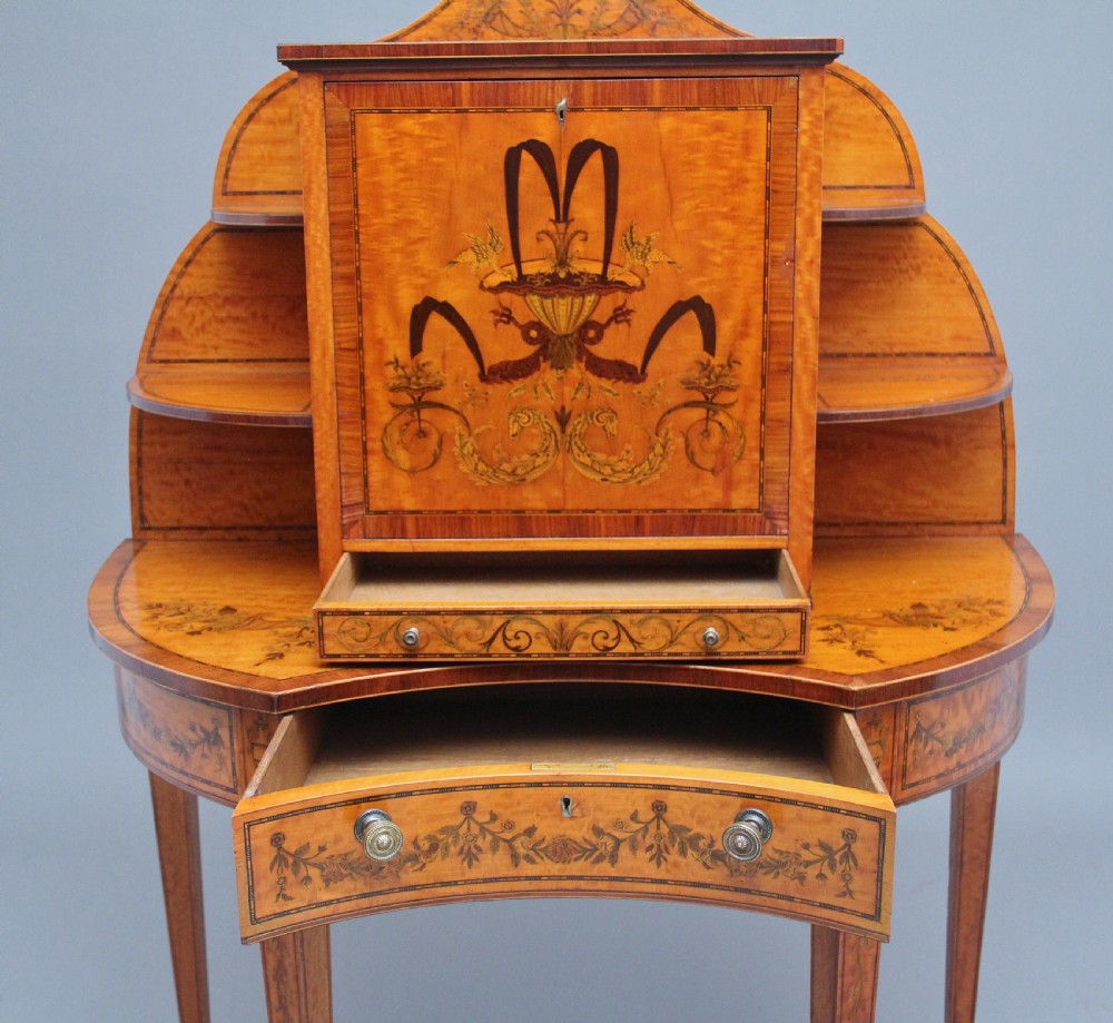 A 19th-century Sheraton revival satinwood writing desk featuring inlaid urn marquetry motifs, stepped side shelves, a central door compartment, and slender tapered legs. View II