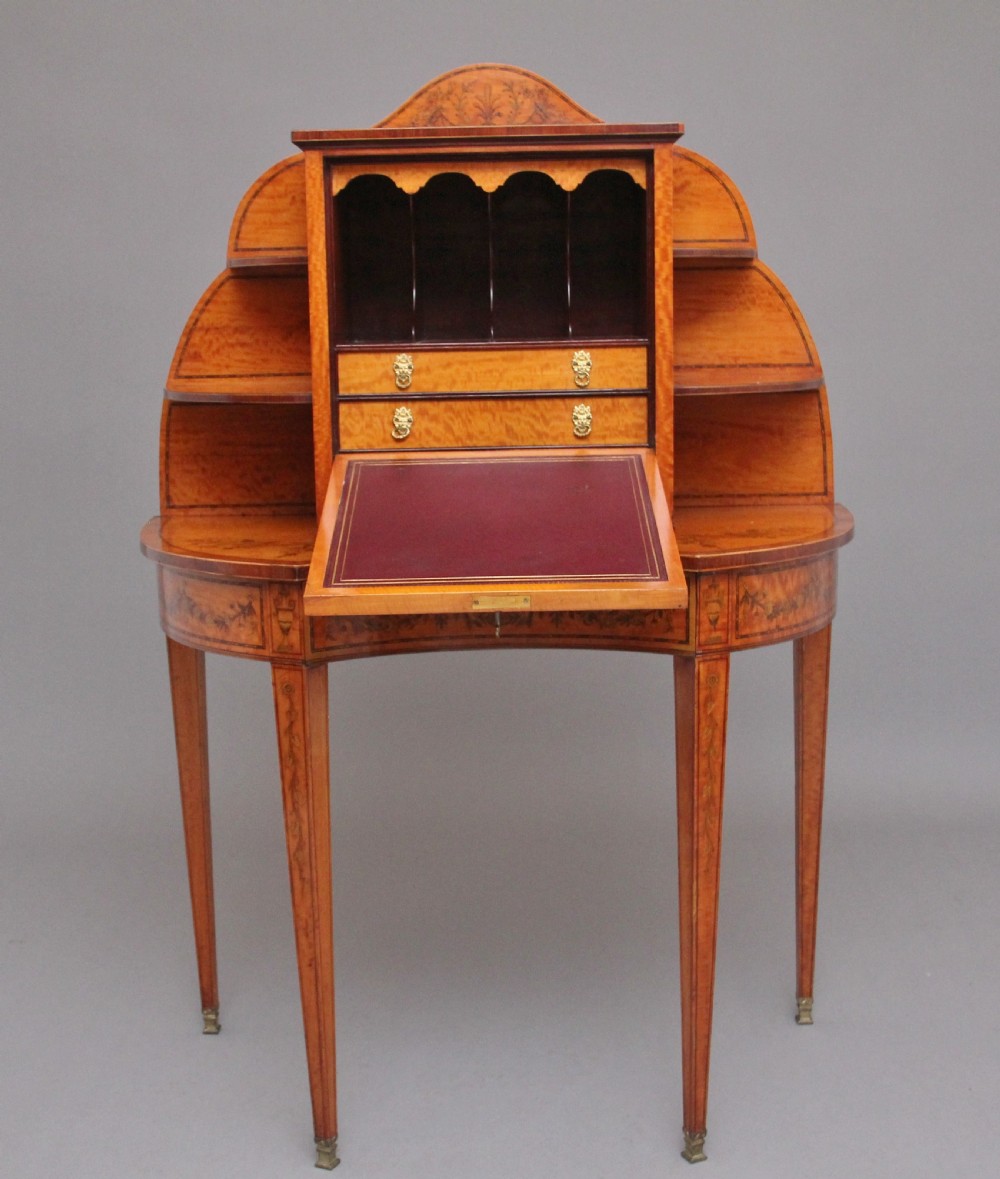 A 19th-century Sheraton revival satinwood writing desk featuring inlaid urn marquetry motifs, stepped side shelves, a central door compartment, and slender tapered legs. View III