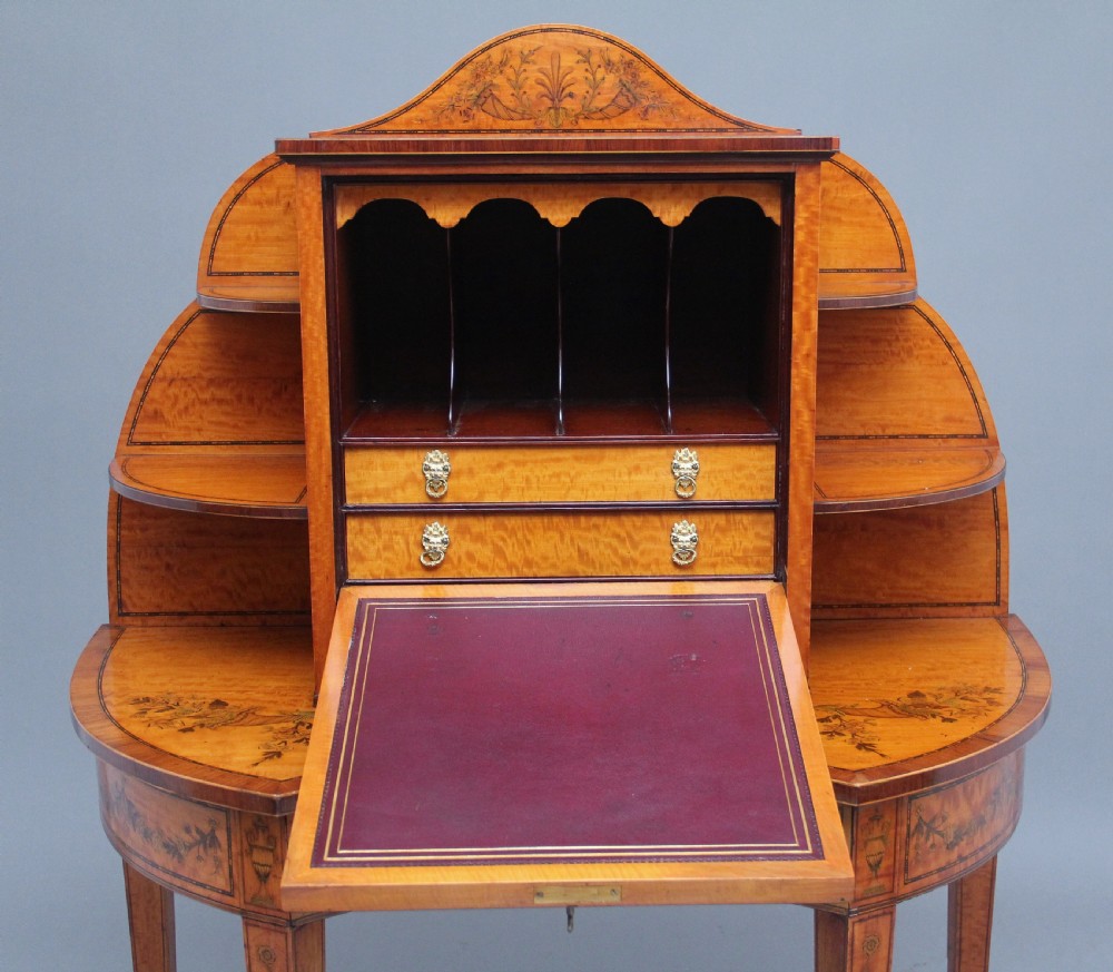 A 19th-century Sheraton revival satinwood writing desk featuring inlaid urn marquetry motifs, stepped side shelves, a central door compartment, and slender tapered legs. View IV