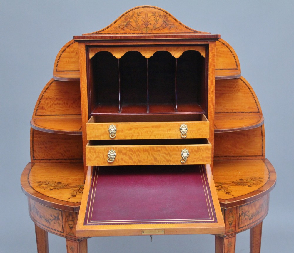 A 19th-century Sheraton revival satinwood writing desk featuring inlaid urn marquetry motifs, stepped side shelves, a central door compartment, and slender tapered legs. View V