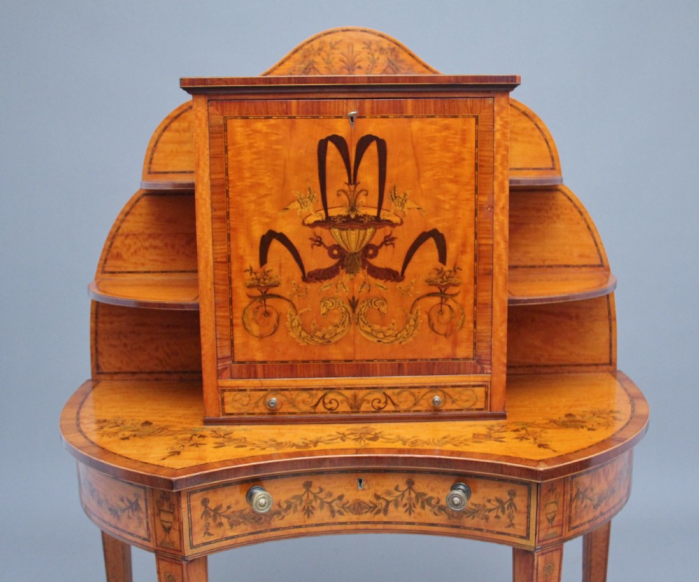 A 19th-century Sheraton revival satinwood writing desk featuring inlaid urn marquetry motifs, stepped side shelves, a central door compartment, and slender tapered legs. View VIII