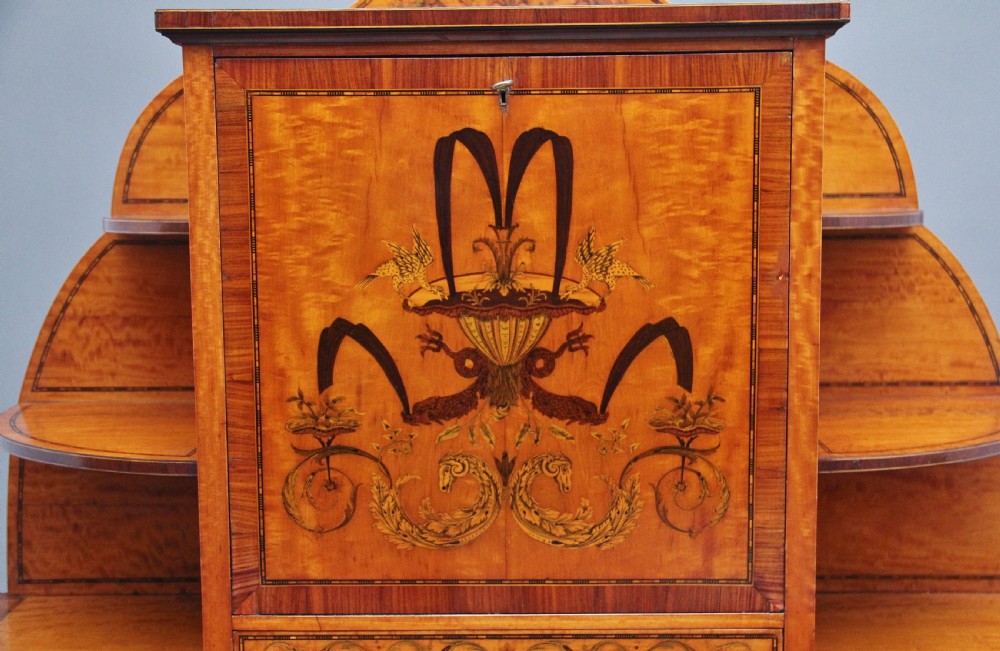 A 19th-century Sheraton revival satinwood writing desk featuring inlaid urn marquetry motifs, stepped side shelves, a central door compartment, and slender tapered legs. View IX