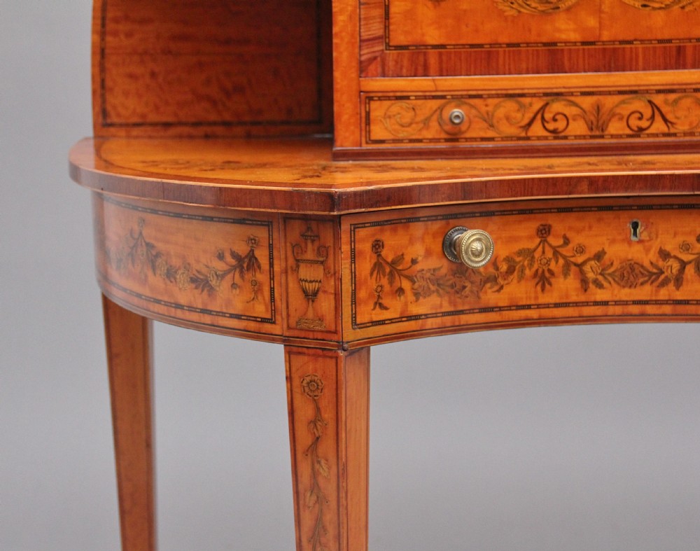 A 19th-century Sheraton revival satinwood writing desk featuring inlaid urn marquetry motifs, stepped side shelves, a central door compartment, and slender tapered legs. View XII