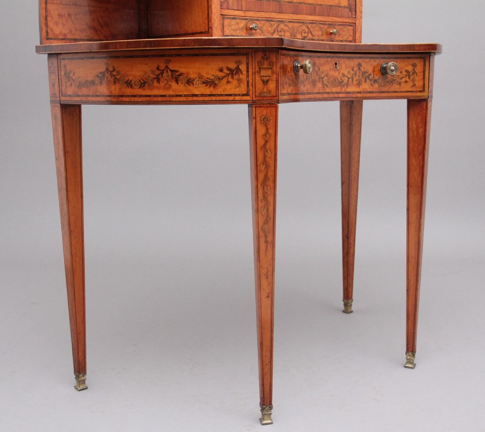 A 19th-century Sheraton revival satinwood writing desk featuring inlaid urn marquetry motifs, stepped side shelves, a central door compartment, and slender tapered legs. View XIII