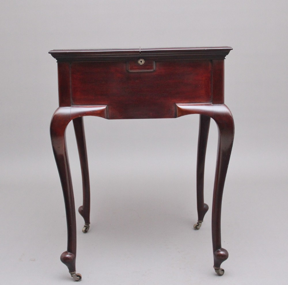 An early 20th-century dark mahogany metamorphic writing desk featuring cabriole legs on brass castors, fold-out side panels, a central leather writing slope, and an integrated clock with stationery compartment. View II