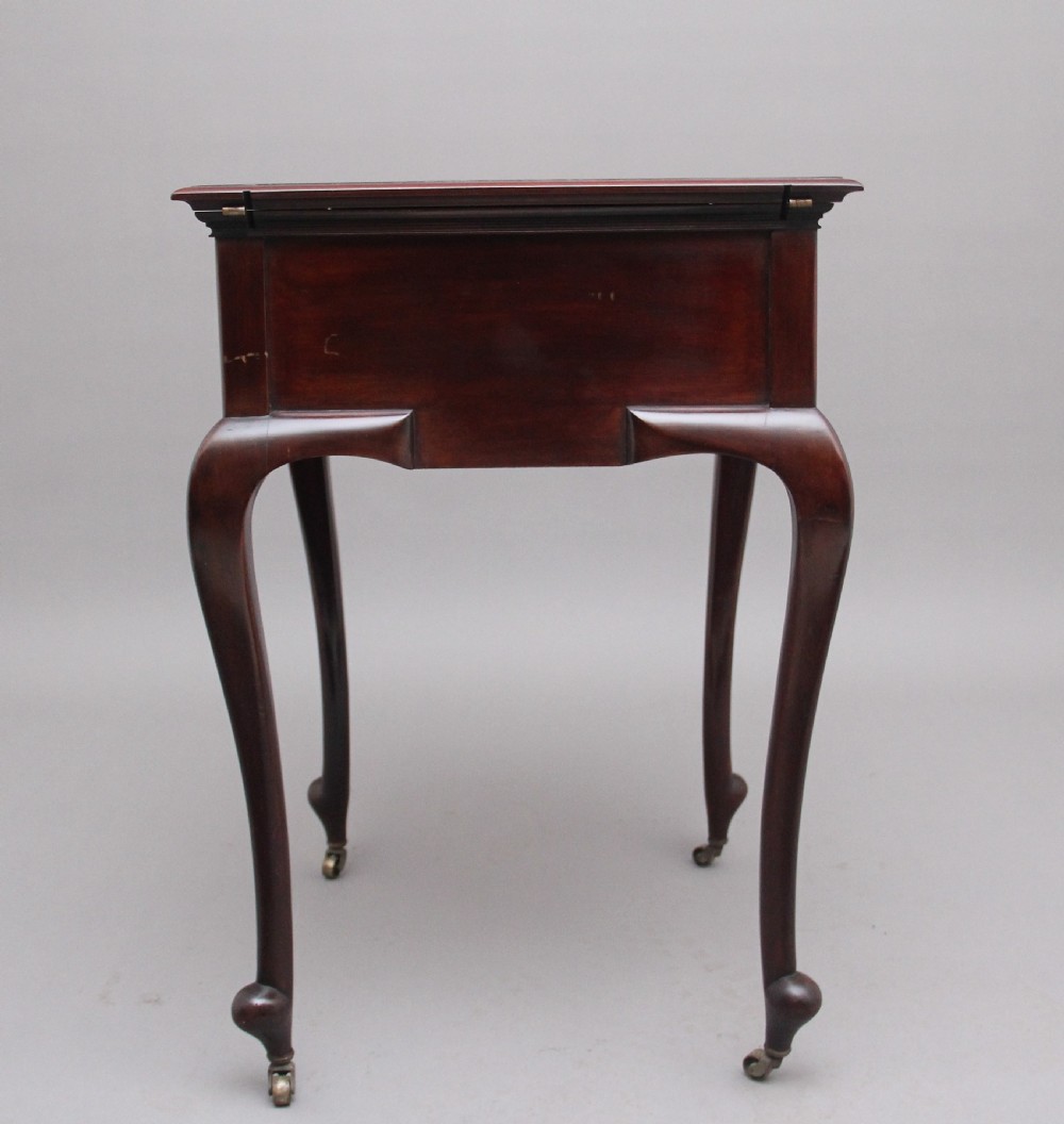 An early 20th-century dark mahogany metamorphic writing desk featuring cabriole legs on brass castors, fold-out side panels, a central leather writing slope, and an integrated clock with stationery compartment. View III