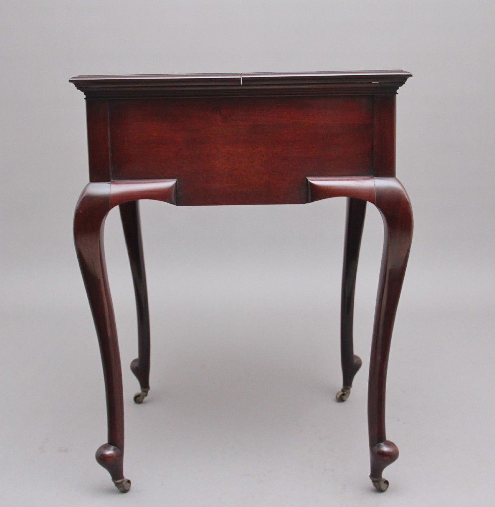 An early 20th-century dark mahogany metamorphic writing desk featuring cabriole legs on brass castors, fold-out side panels, a central leather writing slope, and an integrated clock with stationery compartment. View IV