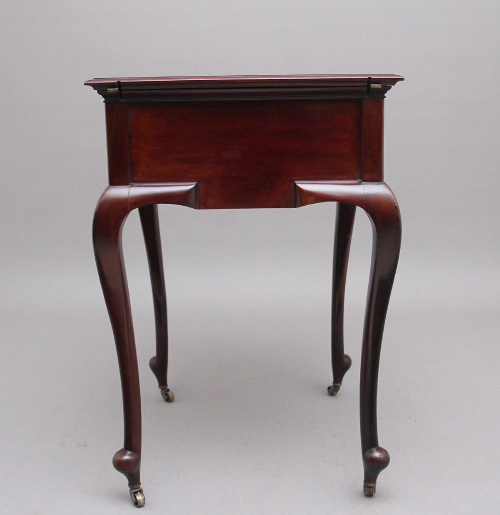 An early 20th-century dark mahogany metamorphic writing desk featuring cabriole legs on brass castors, fold-out side panels, a central leather writing slope, and an integrated clock with stationery compartment. View V