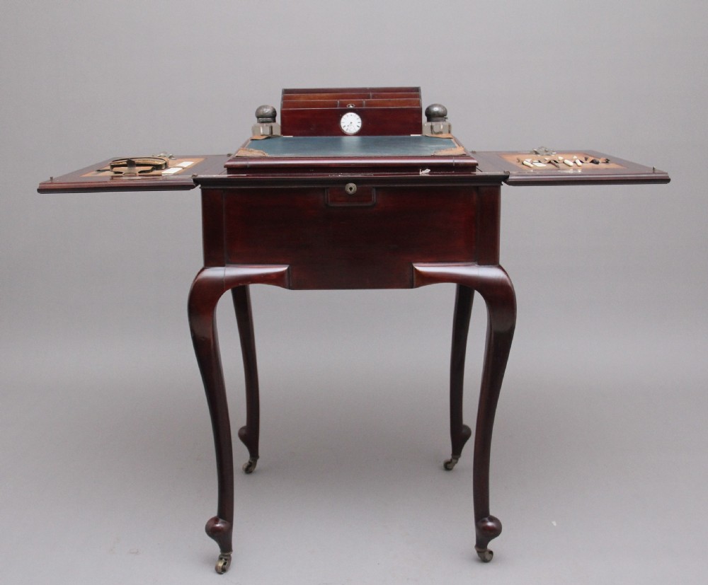 An early 20th-century dark mahogany metamorphic writing desk featuring cabriole legs on brass castors, fold-out side panels, a central leather writing slope, and an integrated clock with stationery compartment. View VII