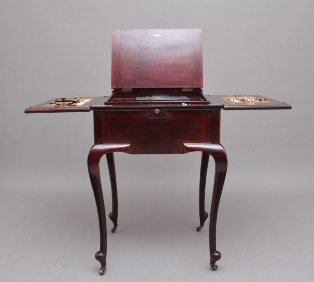 An early 20th-century dark mahogany metamorphic writing desk featuring cabriole legs on brass castors, fold-out side panels, a central leather writing slope, and an integrated clock with stationery compartment. View VIII