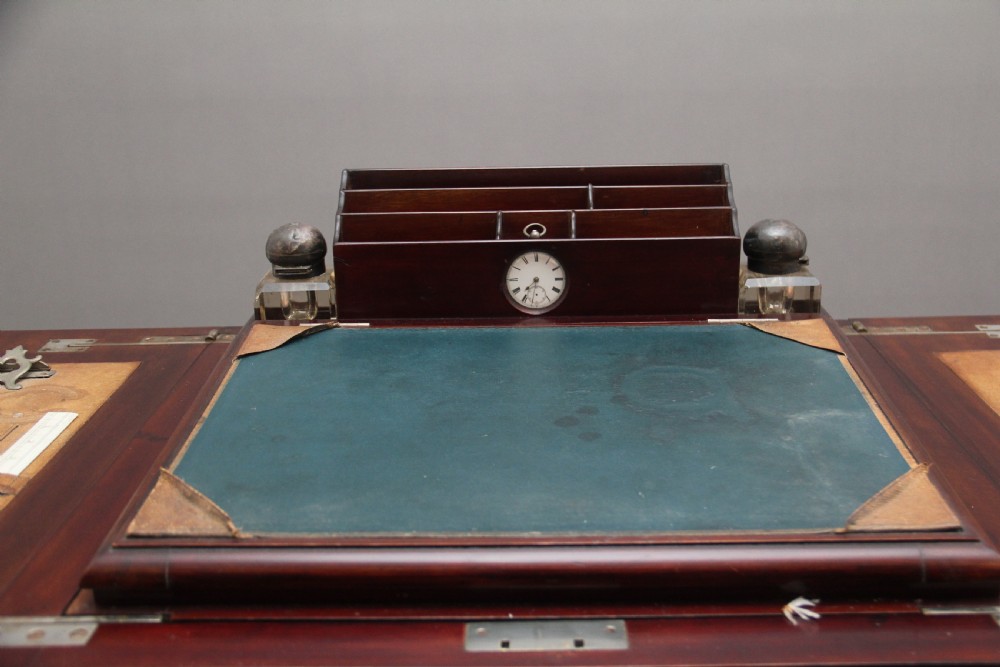 An early 20th-century dark mahogany metamorphic writing desk featuring cabriole legs on brass castors, fold-out side panels, a central leather writing slope, and an integrated clock with stationery compartment. View IX