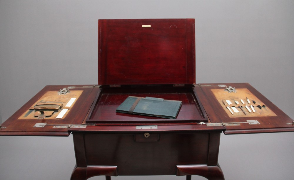 An early 20th-century dark mahogany metamorphic writing desk featuring cabriole legs on brass castors, fold-out side panels, a central leather writing slope, and an integrated clock with stationery compartment. View XI