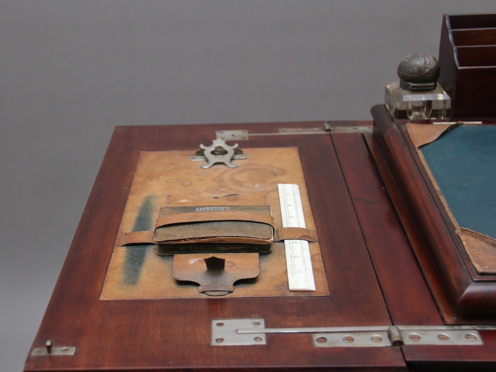 An early 20th-century dark mahogany metamorphic writing desk featuring cabriole legs on brass castors, fold-out side panels, a central leather writing slope, and an integrated clock with stationery compartment. View XII