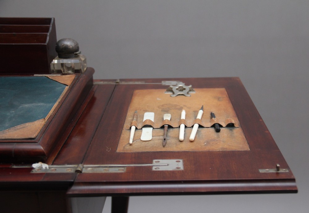 An early 20th-century dark mahogany metamorphic writing desk featuring cabriole legs on brass castors, fold-out side panels, a central leather writing slope, and an integrated clock with stationery compartment. View XIII