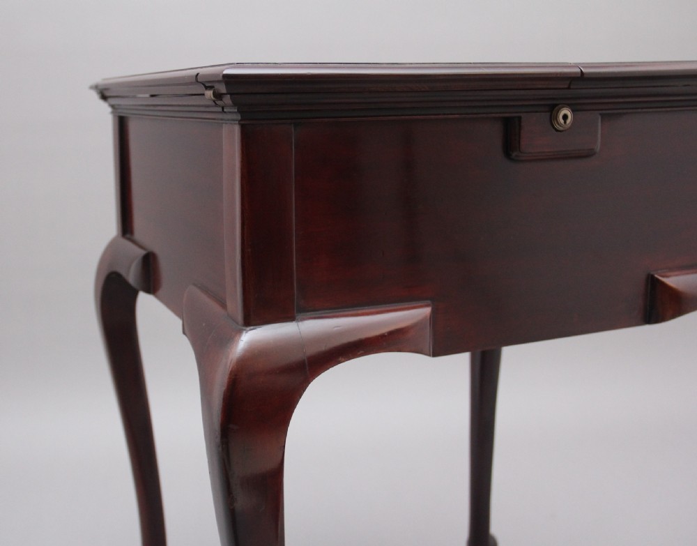 An early 20th-century dark mahogany metamorphic writing desk featuring cabriole legs on brass castors, fold-out side panels, a central leather writing slope, and an integrated clock with stationery compartment. View XV