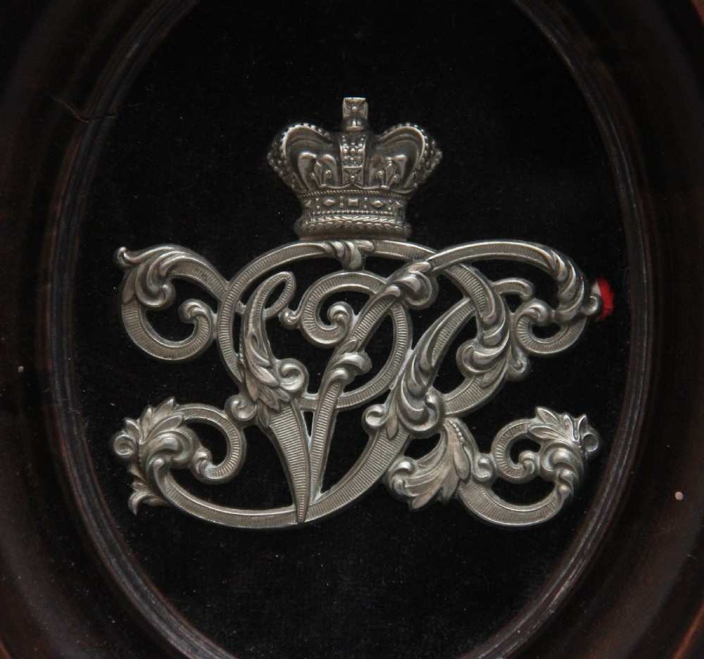 A 19th-century silver-toned royal cypher topped with a crown, mounted on black velvet within an oval dark wood frame. View III