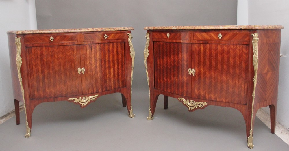 A matching pair of 19th-century French kingwood commodes featuring herringbone parquetry veneer, gilt bronze mounts, and fitted marble tops.
