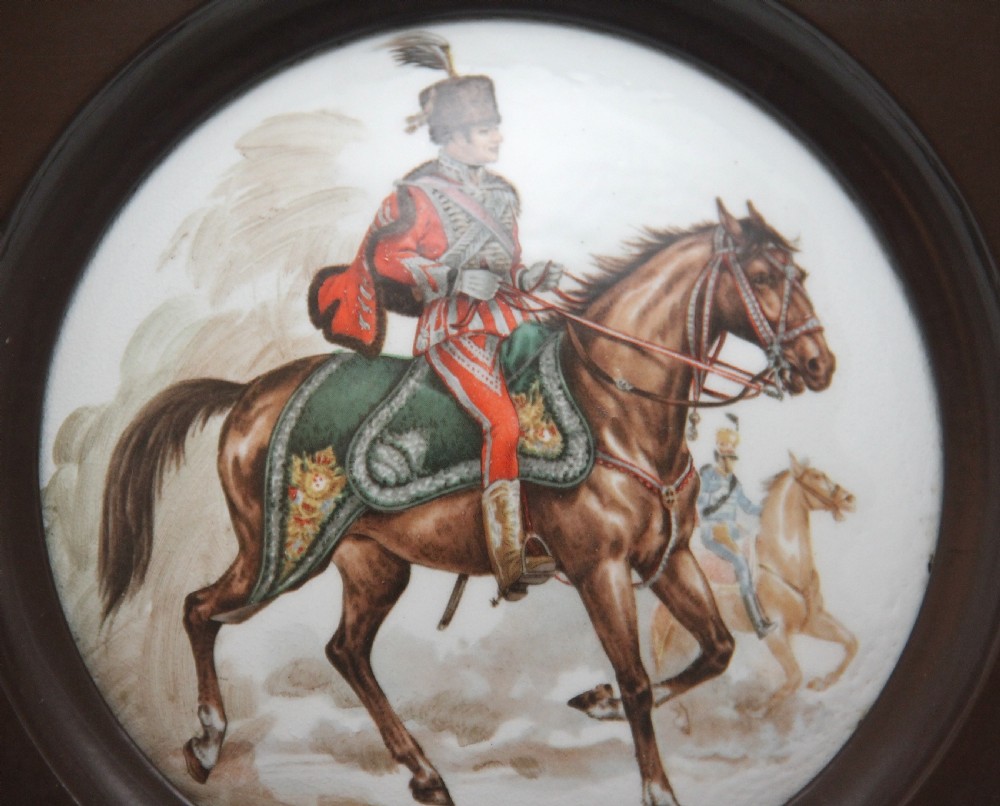 A square dark brown frame enclosing a circular white porcelain plaque depicting a military officer in uniform mounted on a brown horse. View II