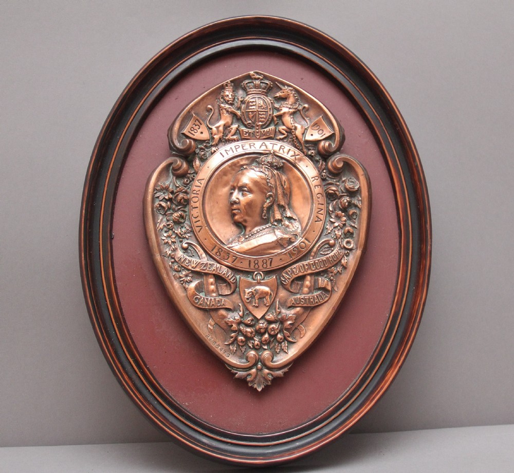 An oval framed copper plaque featuring a raised profile relief of Queen Victoria surrounded by British Royal heraldry and Commonwealth inscriptions.