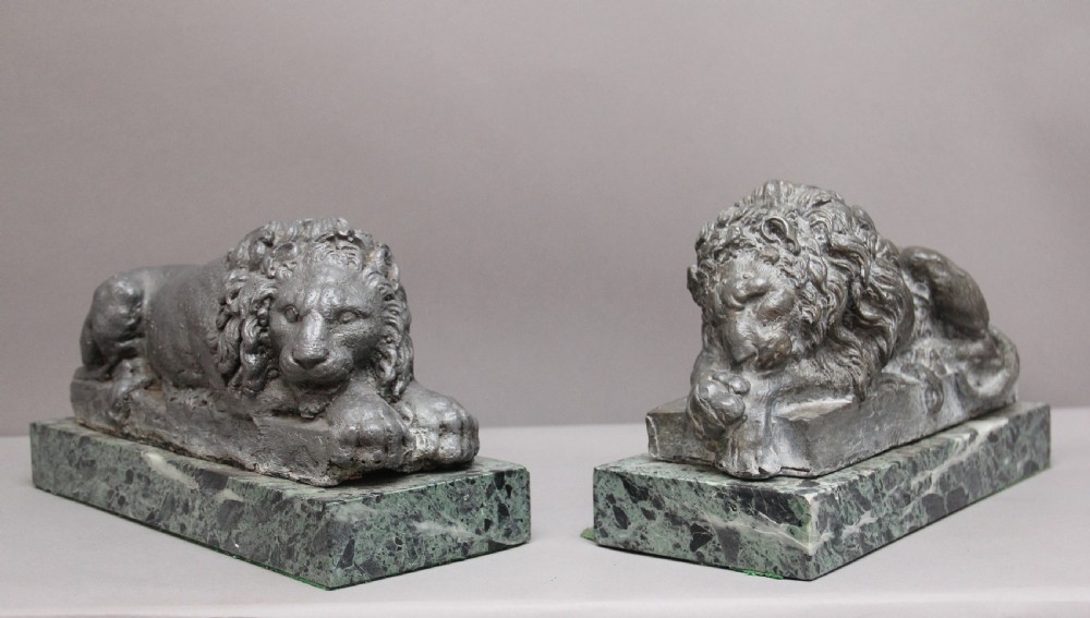 A pair of cast metal reclining lion models, one sleeping and one vigilant, mounted on rectangular green marble bases.