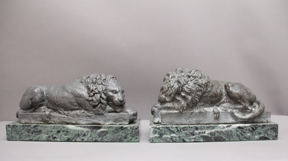 A pair of cast metal reclining lion models, one sleeping and one vigilant, mounted on rectangular green marble bases. View II