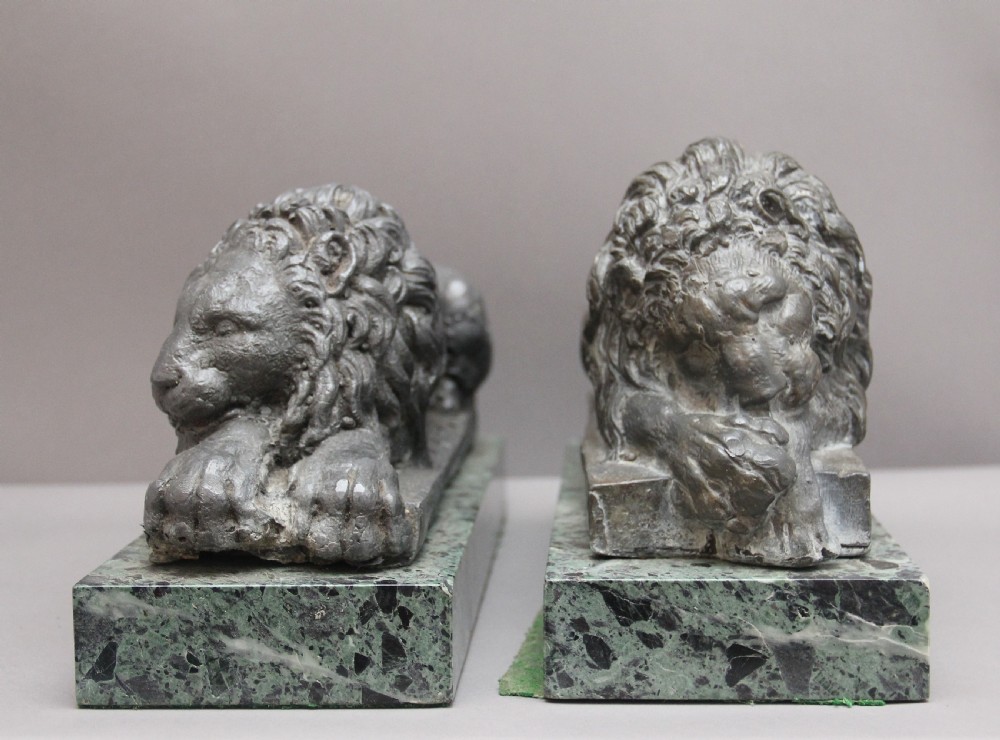 A pair of cast metal reclining lion models, one sleeping and one vigilant, mounted on rectangular green marble bases. View III