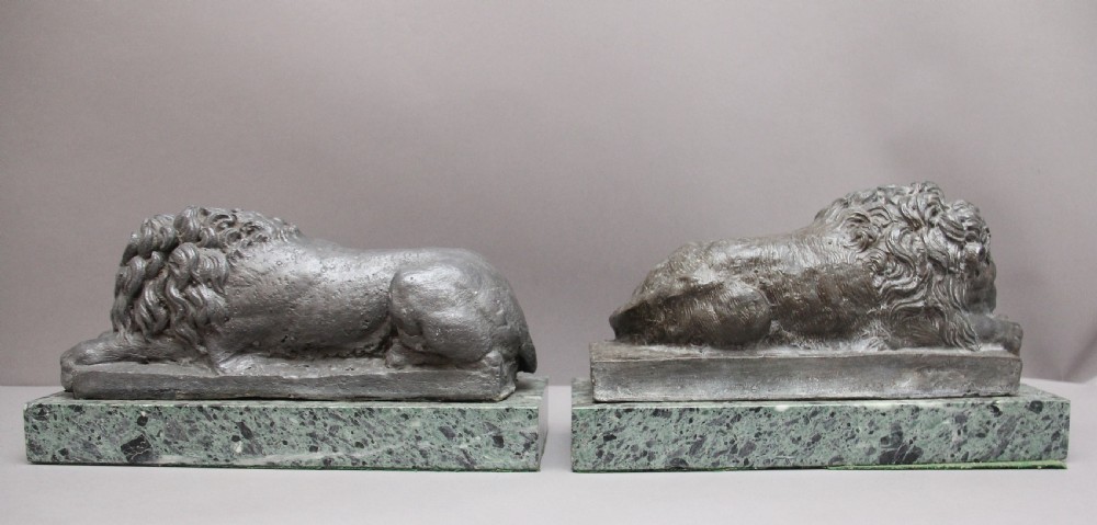 A pair of cast metal reclining lion models, one sleeping and one vigilant, mounted on rectangular green marble bases. View IV