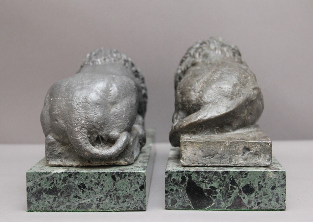 A pair of cast metal reclining lion models, one sleeping and one vigilant, mounted on rectangular green marble bases. View V