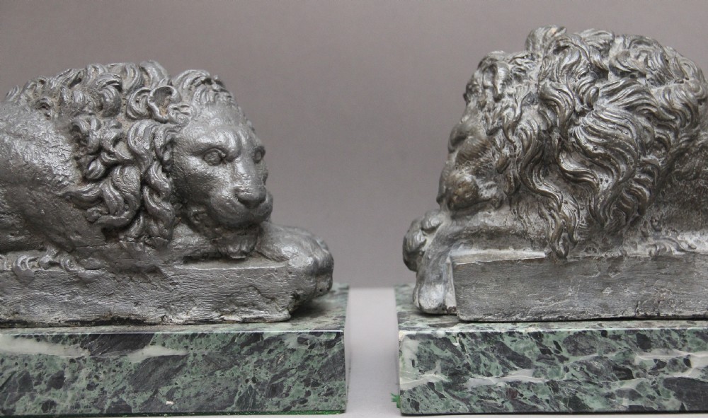 A pair of cast metal reclining lion models, one sleeping and one vigilant, mounted on rectangular green marble bases. View VI