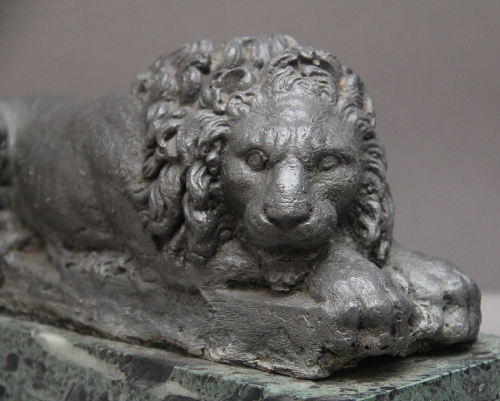 A pair of cast metal reclining lion models, one sleeping and one vigilant, mounted on rectangular green marble bases. View VII