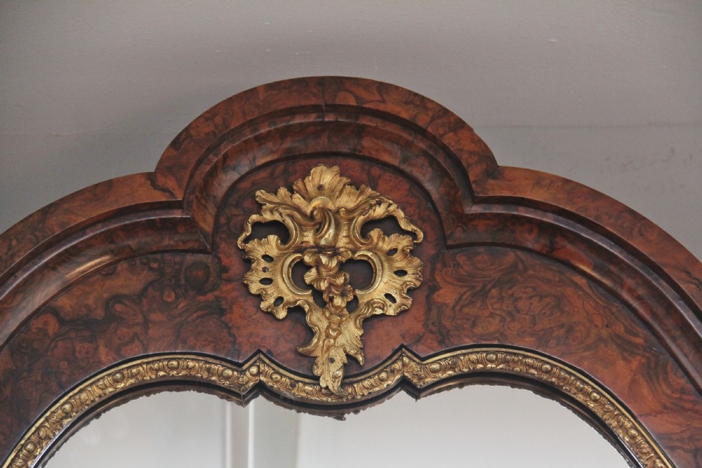 A 19th-century burr walnut credenza with an arched mirror back, ornate gilt-bronze mounts, open tier side shelving, and a central glazed compartment. View IV