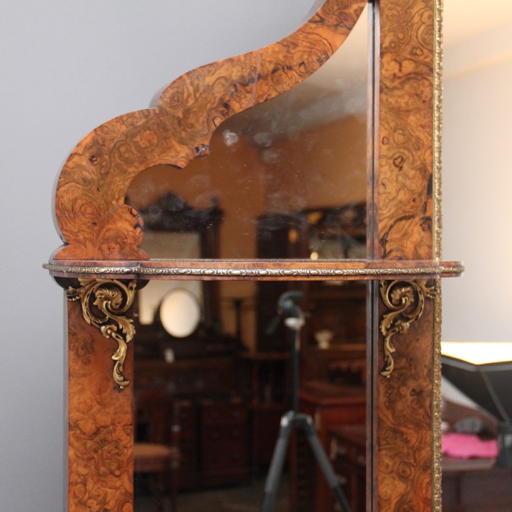 A 19th-century burr walnut credenza with an arched mirror back, ornate gilt-bronze mounts, open tier side shelving, and a central glazed compartment. View VI