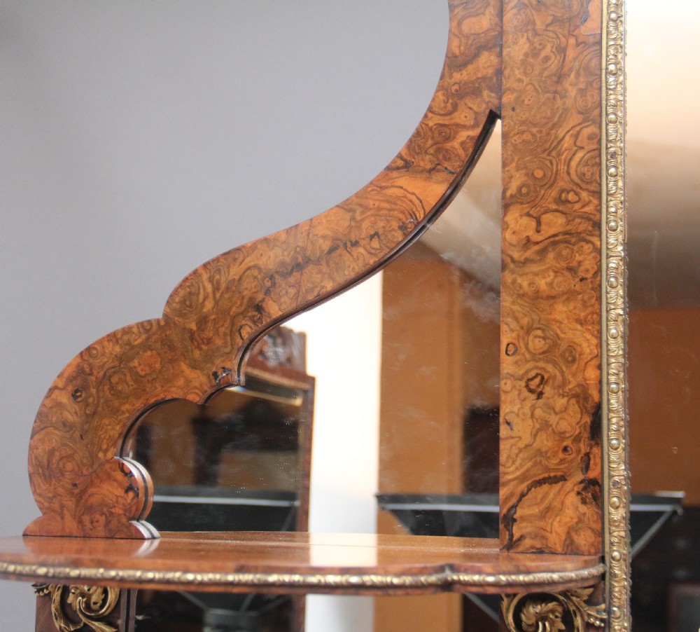 A 19th-century burr walnut credenza with an arched mirror back, ornate gilt-bronze mounts, open tier side shelving, and a central glazed compartment. View X