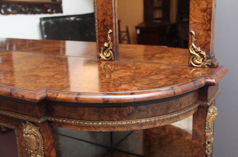 A 19th-century burr walnut credenza with an arched mirror back, ornate gilt-bronze mounts, open tier side shelving, and a central glazed compartment. View XV