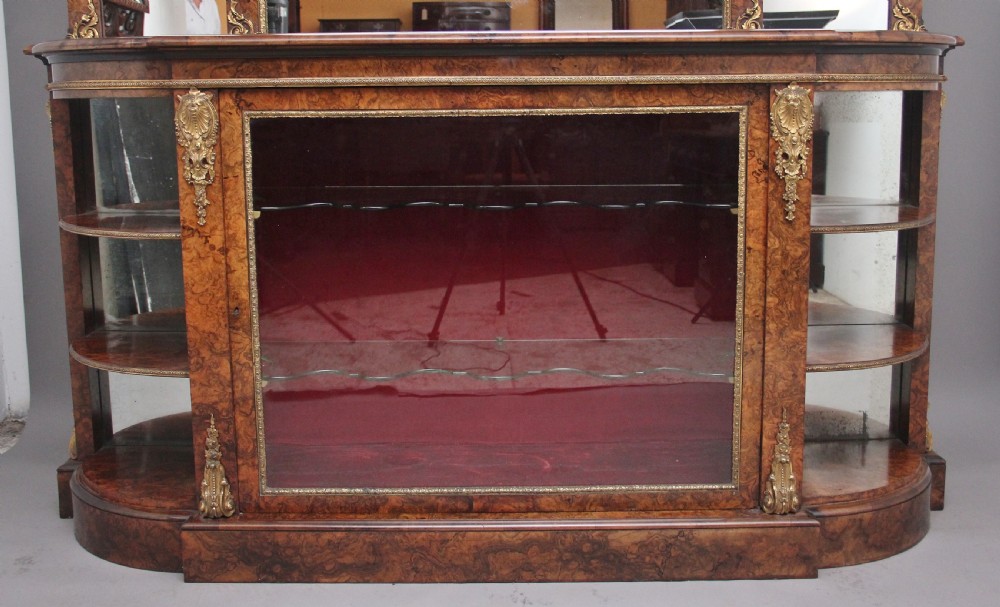 A 19th-century burr walnut credenza with an arched mirror back, ornate gilt-bronze mounts, open tier side shelving, and a central glazed compartment. View XVI