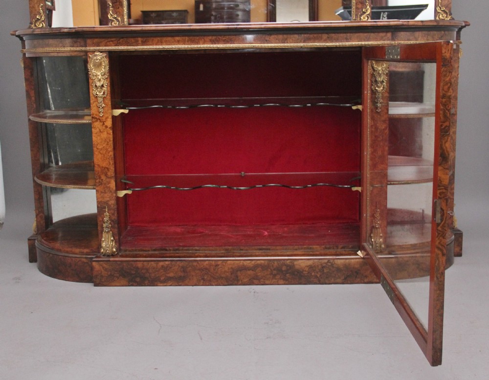A 19th-century burr walnut credenza with an arched mirror back, ornate gilt-bronze mounts, open tier side shelving, and a central glazed compartment. View XVII