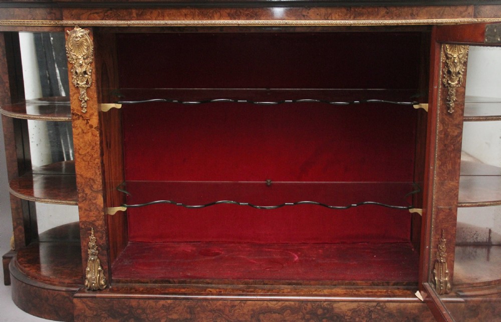 A 19th-century burr walnut credenza with an arched mirror back, ornate gilt-bronze mounts, open tier side shelving, and a central glazed compartment. View XVIII