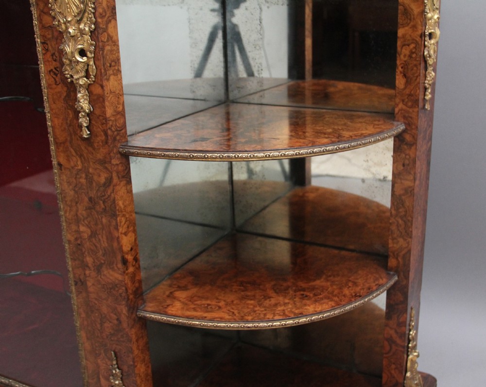 A 19th-century burr walnut credenza with an arched mirror back, ornate gilt-bronze mounts, open tier side shelving, and a central glazed compartment. View XXI