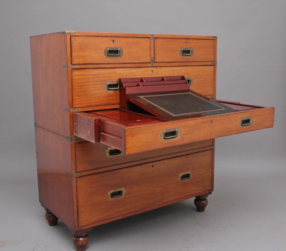 A nineteenth-century mahogany military secretaire chest in two sections with brass corners, flush brass handles, turned feet, and an extended writing drawer.