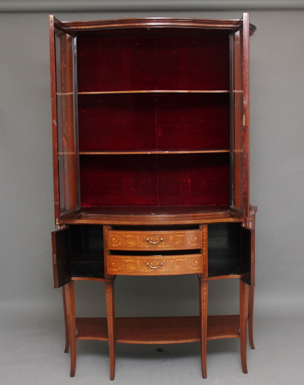 A late 19th-century bow-fronted mahogany display cabinet featuring glazed doors, satinwood marquetry inlay, slender square legs, and an undertier. View III