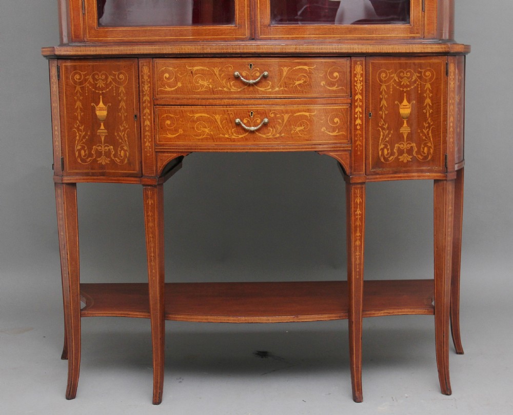 A late 19th-century bow-fronted mahogany display cabinet featuring glazed doors, satinwood marquetry inlay, slender square legs, and an undertier. View IV